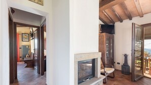 A cozy living area with a stone fireplace, wooden beams, and a view of the outdoors. - Beautiful private villa for 5 people with WIFI, TV, terrace and panoramic view (Roccastrada)