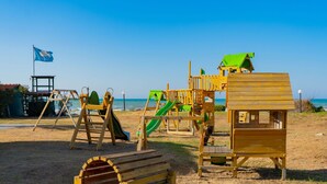A beach playground with swings, slides, and a wooden bench.