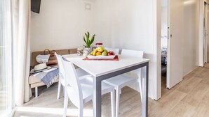 A modern dining area with a white table and chairs, a fruit bowl, and a plant on the table.