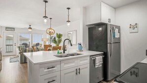 Uma cozinha moderna com armários brancos, geladeira de aço inoxidável e iluminação pendente.