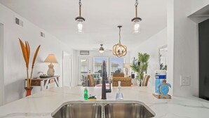 Cozinha moderna com uma ilha grande, pia de aço inoxidável e iluminação pendente.