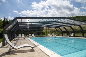 Una piscina con un deck de cristal, sillas de descanso y vistas despejadas del entorno verde.