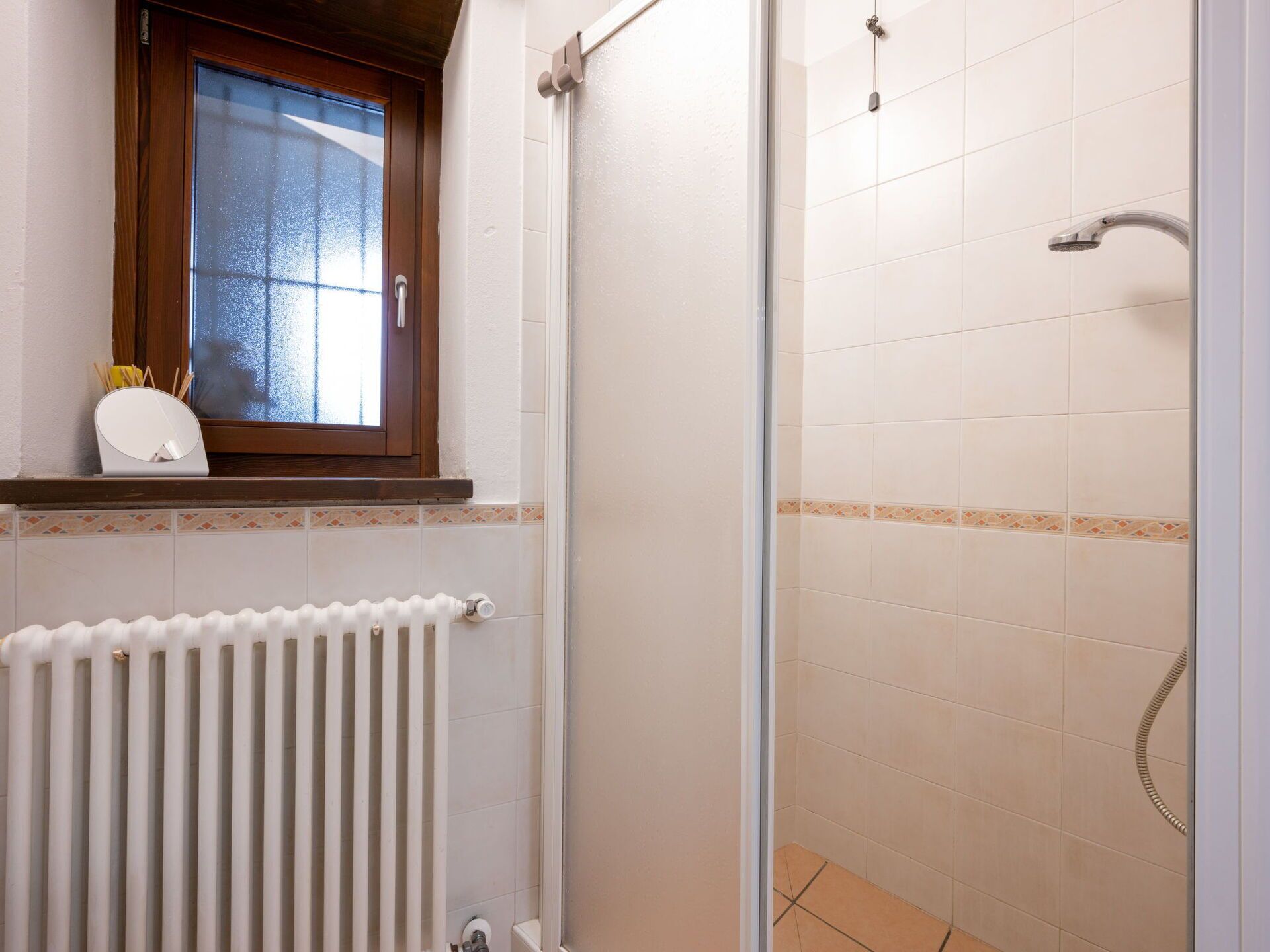 A bathroom with a shower, a window, and a radiator.