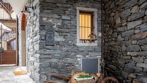 A stone building with a window, a wooden cart with firewood, and a metal bell. - Wonderful  villa for 2 guests with A/C, WIFI and TV (Mergozzo)
