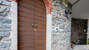 A stone building with a large wooden door, a stone wall, and a small outdoor area with a stone floor and a doormat. - Wonderful  villa for 2 guests with A/C, WIFI and TV (Mergozzo)