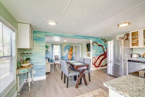 Un comedor con mesa y sillas, una cocina con refrigerador y armarios, y un mural en la pared.
