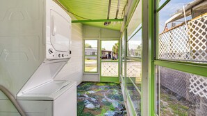 Un lavadero con lavadora, techo verde y vista al exterior por una ventana.