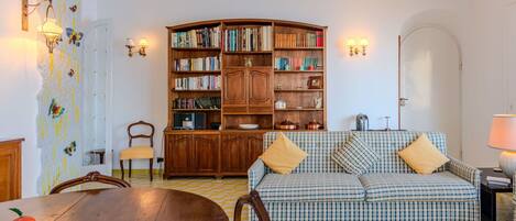 A cozy living room with a checkered sofa, a wooden bookshelf, and a dining table with fruit.