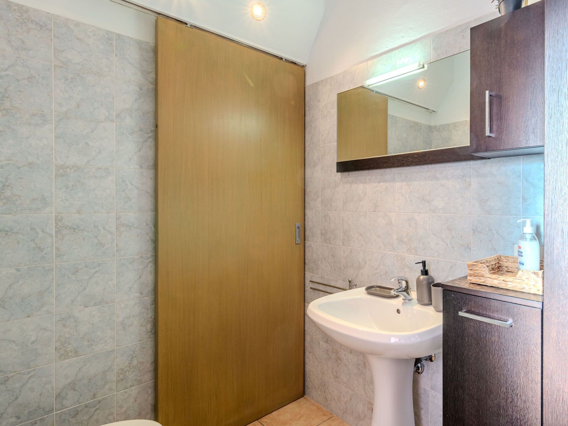 A bathroom with a wooden door, a white sink, and a mirror above it.