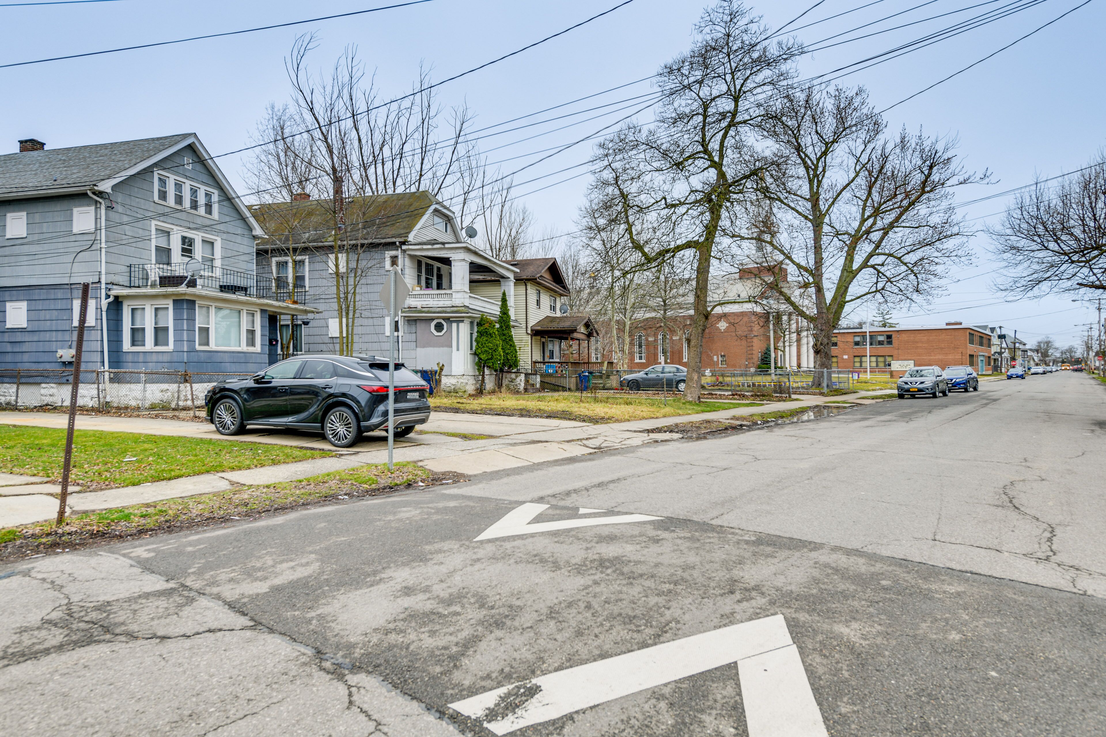 Une rue résidentielle bordée de maisons, avec des voitures garées et une chaussée dégagée.