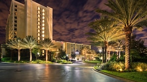 A hotel with multiple floors, a well-lit entrance, and palm trees lining the driveway. - Orlando | Easy Disney Retreat | Pool + Parks (Orlando)