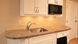 A kitchen with a granite countertop, stainless steel sink, white cabinetry, a black microwave, and a dishwasher. - Orlando | Easy Disney Retreat | Pool + Parks (Orlando)