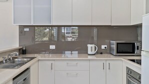 A modern kitchen with white cabinets, a stainless steel sink, a kettle, a microwave, and an oven. - Yarrawonga Lakeside Apartment 23 (Mulwala)