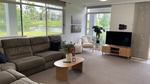 A living room with a large window, a sofa, a coffee table, a TV, and a chair. - Yarrawonga Lakeside Apartment 23 (Mulwala)