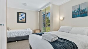 A hotel room with a large bed, a smaller bed, a painting, and a window with a view of greenery. - Yarrawonga Lakeside Apartment 23 (Mulwala)