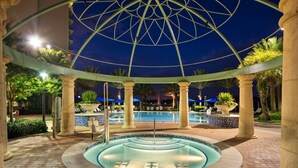 A circular pool with a glass bottom, surrounded by palm trees and columns, under a glass dome structure.