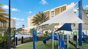Un terrain de jeux avec des toboggans et une piscine en arrière-plan.