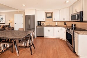 A modern kitchen with white cabinets, stainless steel appliances, and a dining area with a dark table and patterned chairs. - Orlando | Family Park Retreat | Pool + Parks | 2BR (Orlando)
