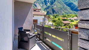 A balcony with a wicker chair and table, overlooking a mountainous landscape with houses. - Lovely apartment for 3 guests with A/C, WIFI and balcony (Novate Mezzola)