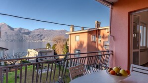 A balcony with a table and a bowl of fruit, overlooking a lake and mountains. - Lovely apartment for 6 guests with WIFI, TV and patio (Germignaga)