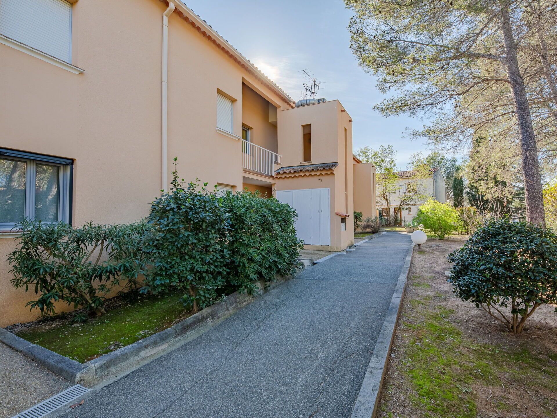Un edifici residencial amb un camí empedrat, una entrada tancada i vegetació als voltants.