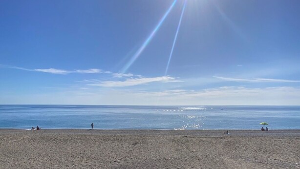 Una playa con gente tomando el sol y un cielo despejado.