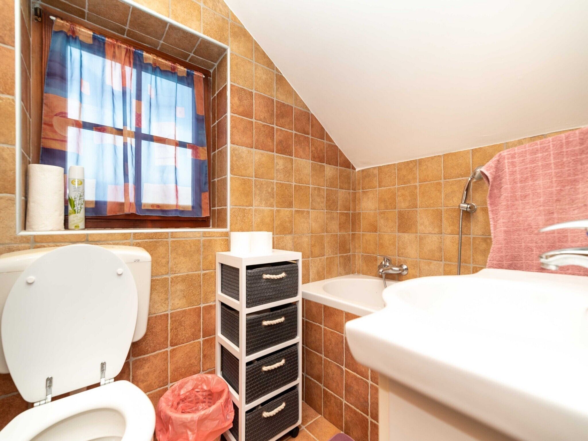 Un baño con inodoro, lavamanos, bañera y ventana con cortinas.