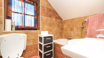 Un baño con inodoro, lavamanos, bañera y ventana con cortinas.