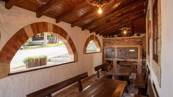 Un interior rústico con vigas de madera, paredes de ladrillo y un horno de leña. Hay bancos y mesas para sentarse.