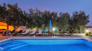 A swimming pool with lounge chairs and umbrellas, surrounded by trees and a building.