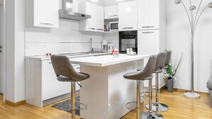 Een moderne keuken met witte kastjes, een centraal eiland met barstoelen, roestvrijstalen apparatuur en hanglampen.