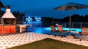 Een terras buiten met een barbecue, zitplaatsen en een neonbord voor 'Dom & San Holiday House'.