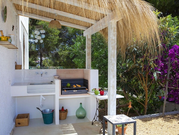 Enjoy al fresco dining with a grill, sink, and table amidst lush greenery and vibrant flowers.