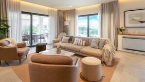 Ein modernes Wohnzimmer mit einer Sofagarnitur, einem Couchtisch und einem Essbereich, der durch große Fenster einsehbar ist.
