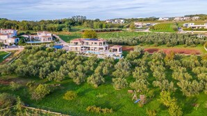 Ein großes, modernes Haus mit Schwimmbad, umgeben von üppiger Vegetation und Olivenbäumen.