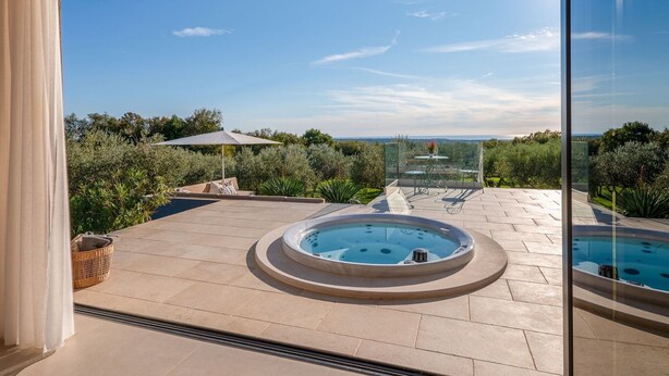 Ein luxuriöser Außenbereich mit Whirlpool, einem Esstisch mit Stühlen und freiem Blick auf die umliegende Landschaft.