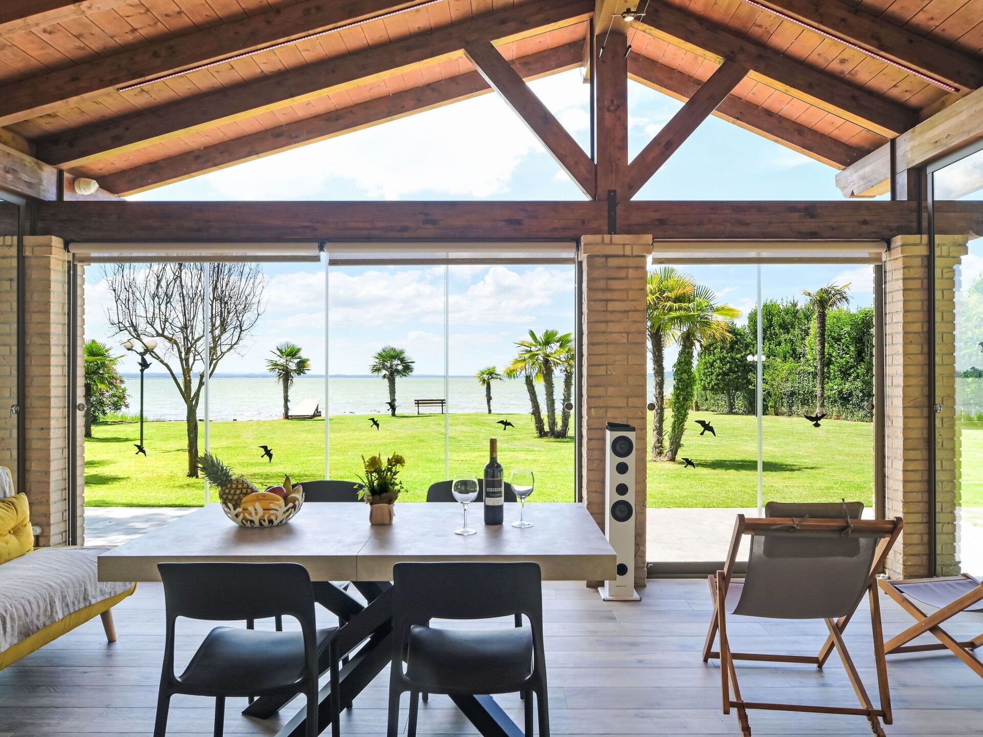 A spacious room with a large table, chairs, and a view of a grassy area with palm trees and a body of water.