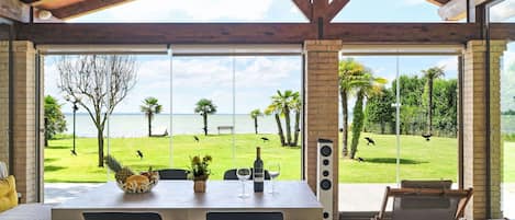 A spacious room with a large table, chairs, and a view of a grassy area with palm trees and a body of water.