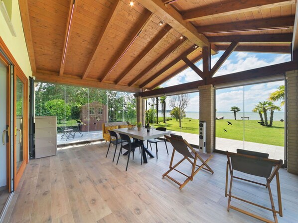 A spacious room with a wooden ceiling and large windows overlooking a grassy area and water.