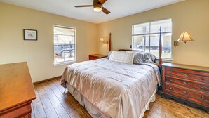 Een slaapkamer met een bed, een houten dressoir, nachtkastjes en een plafondventilator.