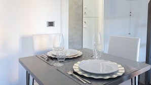 Uma mesa de jantar posta com pratos, talheres e copos, com um armário branco e um aplique na parede ao fundo.