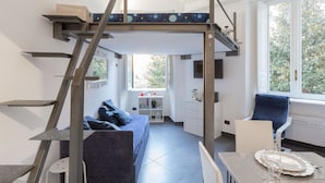 Quarto compacto e moderno com cama beliche, sofá, mesa de jantar e cozinha.