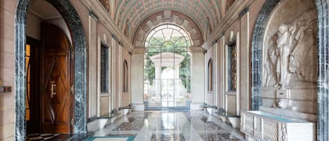A grand hallway with a high arched ceiling, marble flooring, and classical statues.