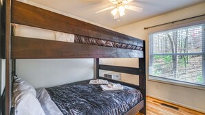 Una cama individual superpuesta con ventilador de techo, una ventana con persianas y una mesita de noche.