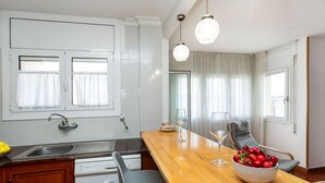 Eine moderne Küche mit einer Holzausziehtafel, zwei Stühlen, einer Obstschale und einem Weinglas.