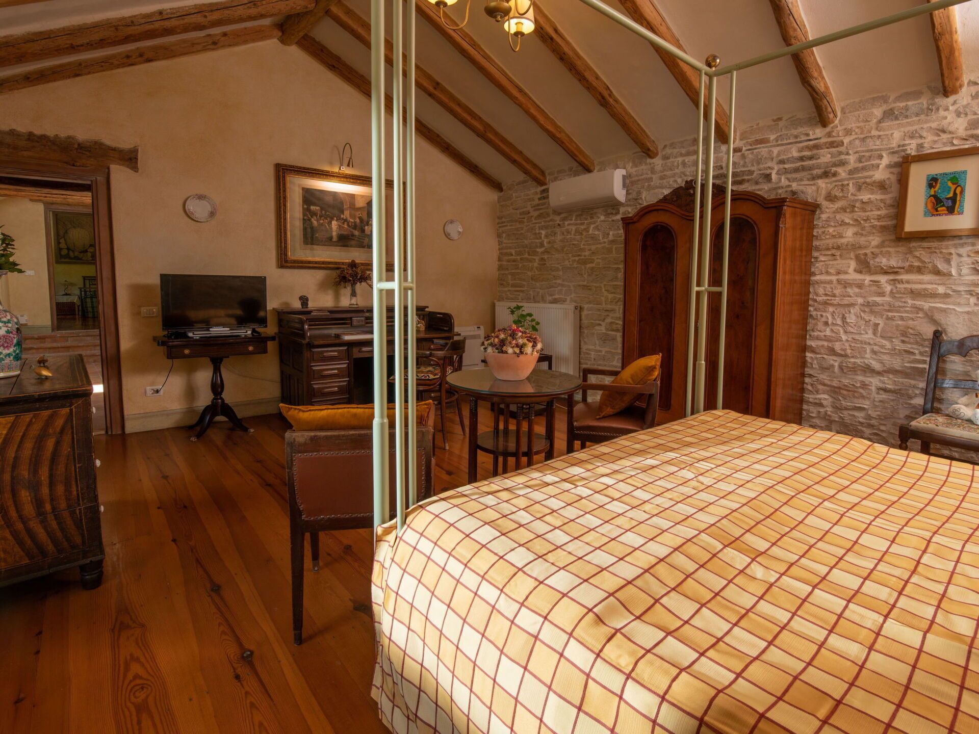 A bedroom with a bed, wooden furniture, a desk, and a stone wall.