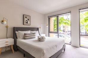 Une chambre moderne avec un grand lit, des tables de chevet, une lampe fixée au mur et une fenêtre donnant sur la rue.