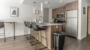 A modern kitchen with a central island, bar stools, a microwave, a refrigerator, and a clock on the wall. - 1BR+Den | Gym | Bellevue | Sophari Downtown D (Bellevue)