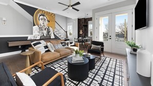 A modern living room with a large mural, a ceiling fan, and a view to the outdoors. - | Downtown Nash | Outlaw Theme | Large Groups | (Nashville)