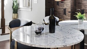 A dining area with a round marble table, black upholstered chairs, a guitar on the wall, and a bottle of wine. - | Downtown Nash | Outlaw Theme | Large Groups | (Nashville)